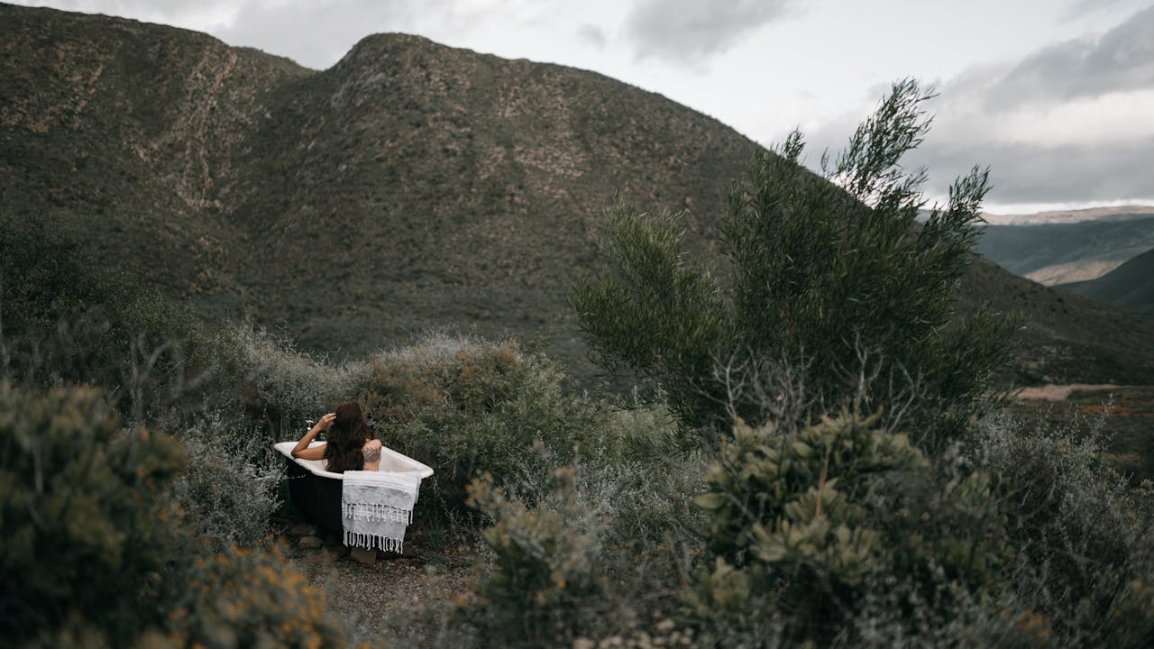 A woman relaxes in a bathtub amidst lush mountain scenery, showcasing tranquility and nature.